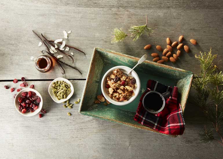 A bowl of Morning Summit cereal on a tray with pumpkin seeds, whole almonds, and dried cranberries