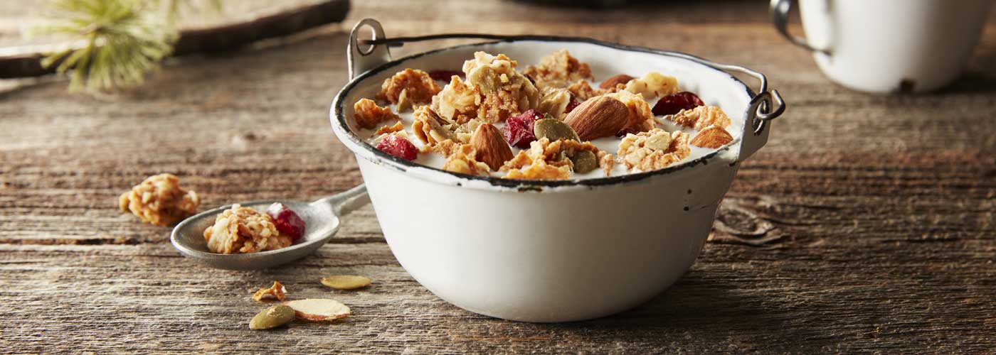 A white metal bowl filled with Morning Summit cereal with whole almonds and dried cranberries