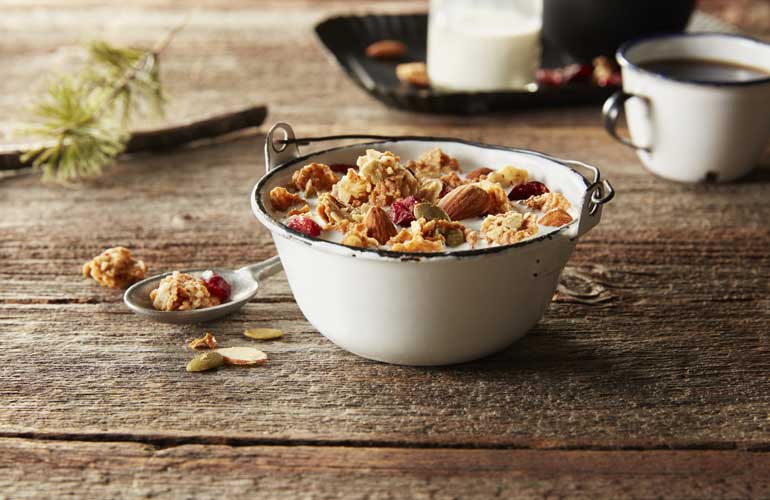 A white metal bowl filled with Morning Summit cereal with whole almonds and dried cranberries